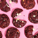 Red Velvet New York Cookie with white chocolate chips, freshly baked by Crumbs & Doilies, on a bright pink background.